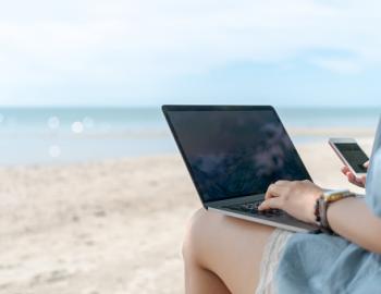 young woman on laptop while sitting on beach working remotely