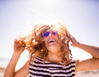 young woman in sunshine with sunglasses and wind in hair